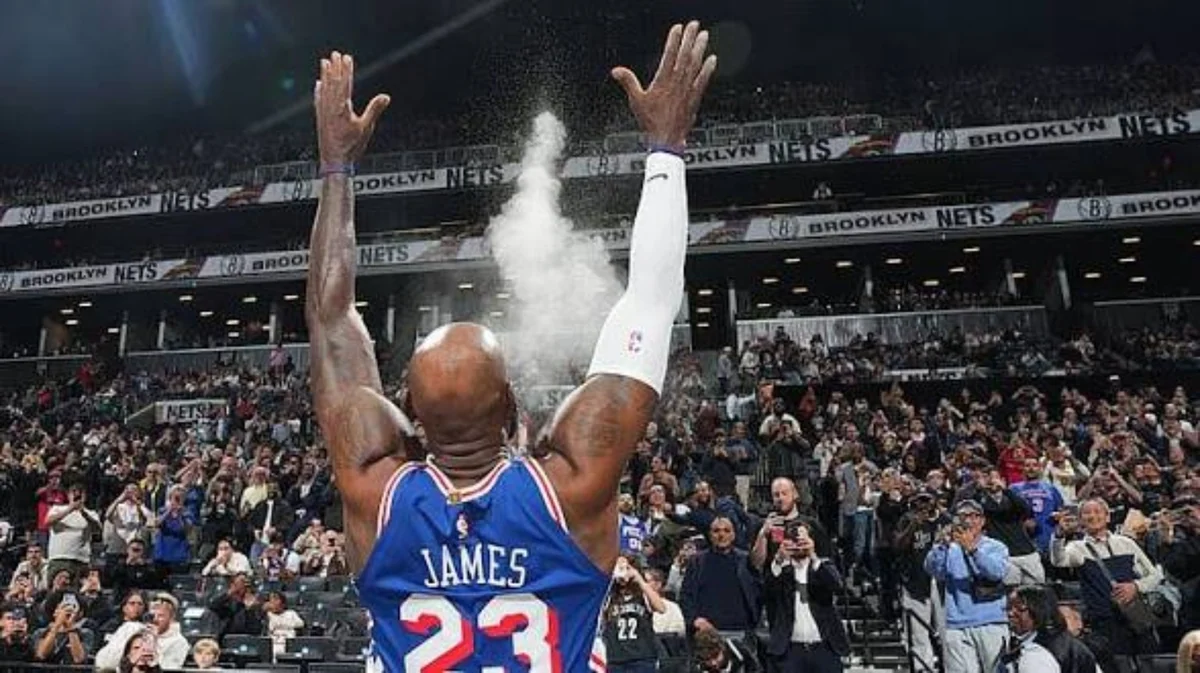 LeBron James wearing a blue Philadelphia 76ers jersey celebrating with both arms raised