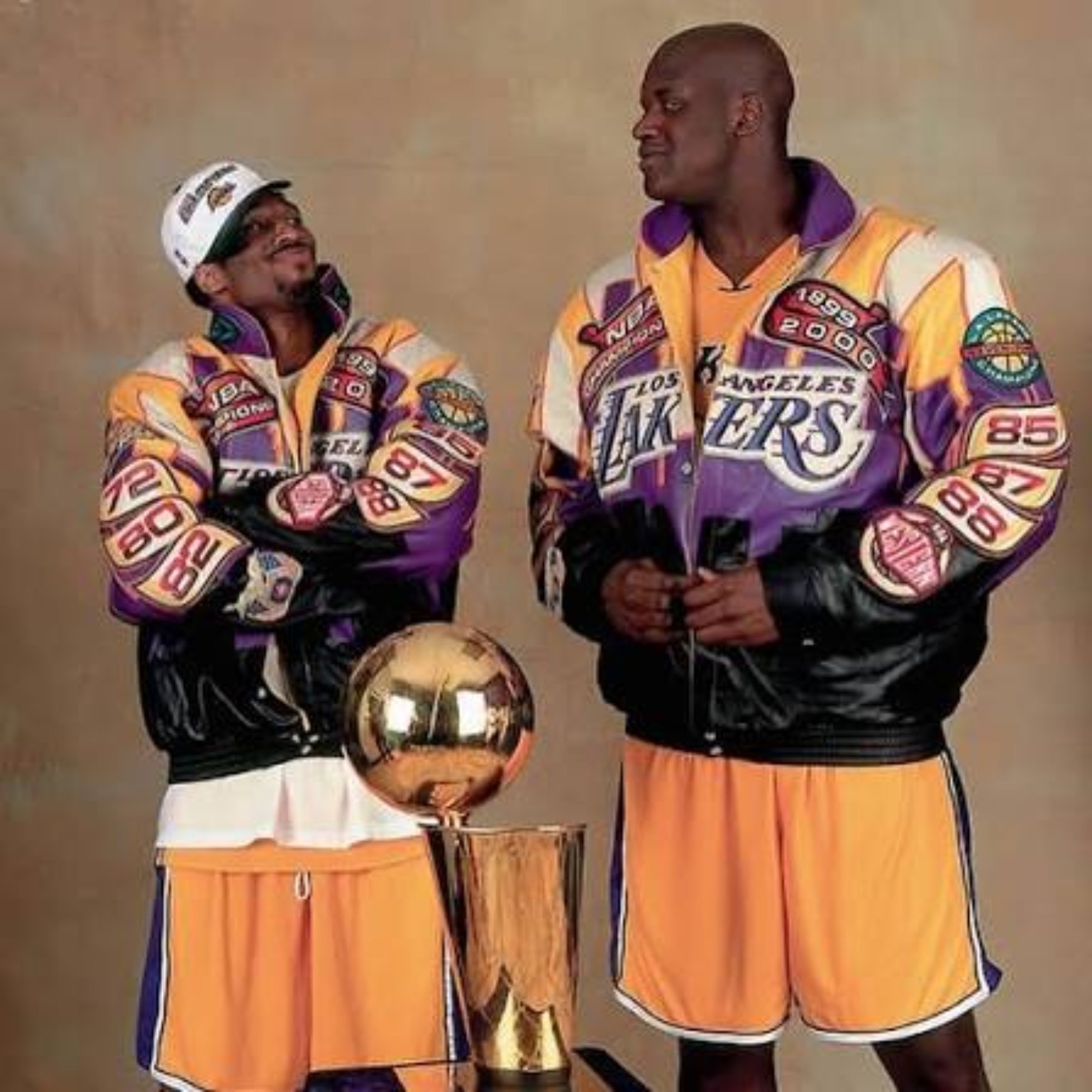 Kobe Bryant and Shaquille O'Neal in Lakers championship gear beside the NBA championship trophy